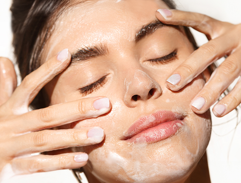 Frau mit geschlossenen Augen reinigt ihr Gesicht mit Reinigungsschaum.